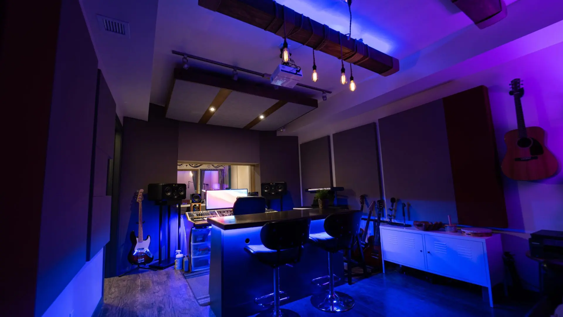 This is the control room in studio A at Made Human Studios Toronto. It features large ceilings, sound panels, guitars on the walls, with a central producers island for people to sit at behind the audio engineer. There is a glass wall looking into the studios live room.